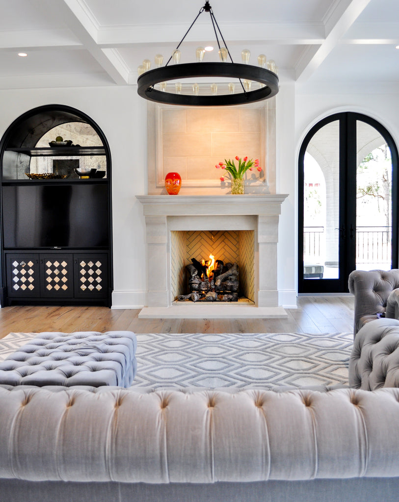 living room with gray sofa, ottoman, blue and white rug, fireplace, shelving, and chandelier